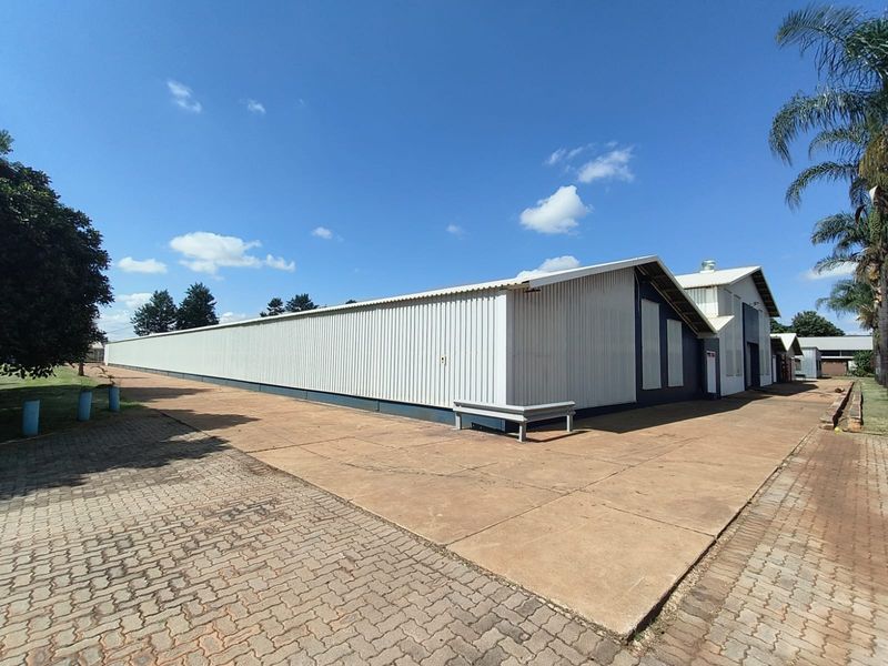 Exterior view of a large industrial warehouse building featuring corrugated metal cladding, a concrete apron, and paved driveway access.