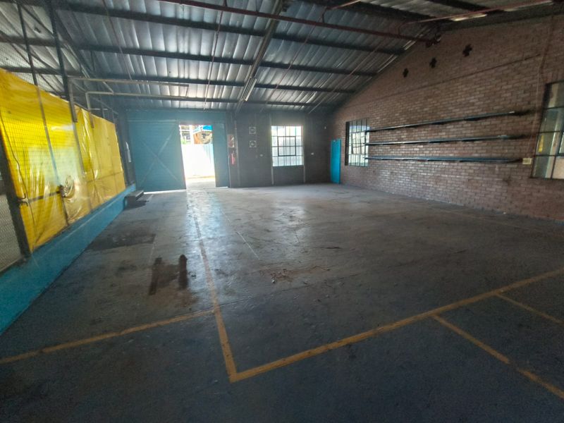 Spacious industrial utility area featuring exposed brick walls, concrete flooring, high-pitched metal roof, and large sliding access door.