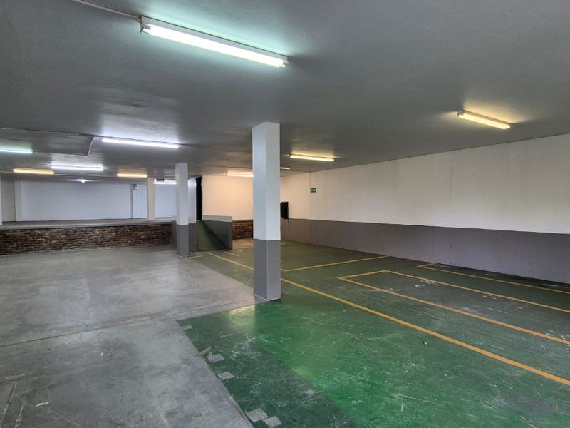 Spacious industrial garage area featuring concrete flooring with painted markings, structural support columns, and overhead fluorescent lighting.