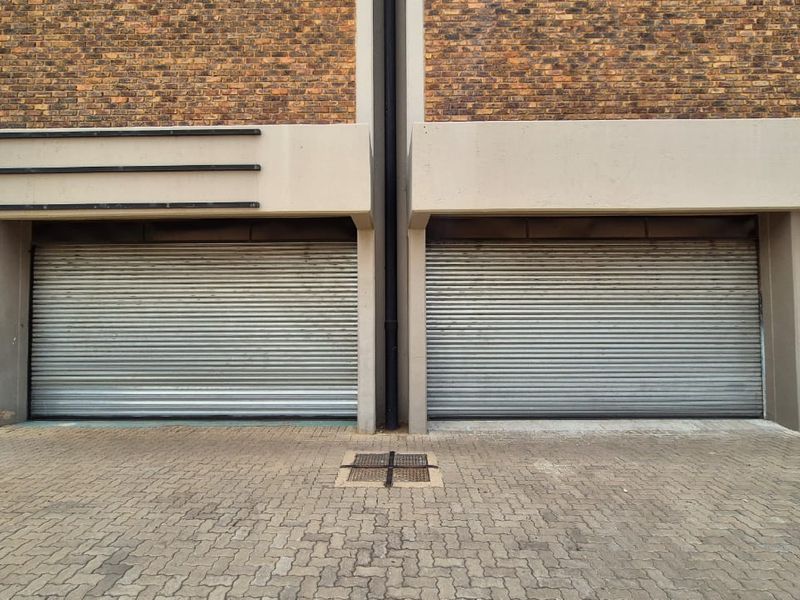 Industrial property exterior featuring multiple metal roller shutter doors, brick facade, and paved driveway access.