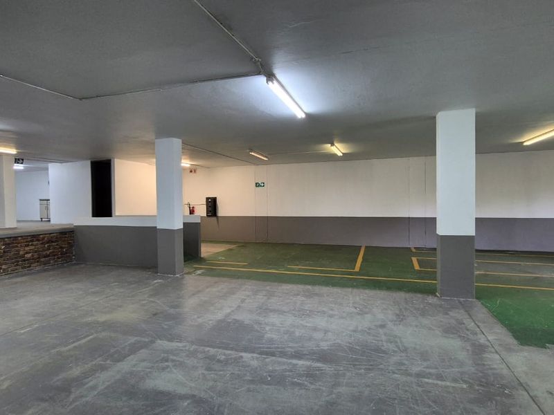 Spacious industrial garage area featuring concrete flooring with marked parking bays, structural columns, and overhead fluorescent lighting.