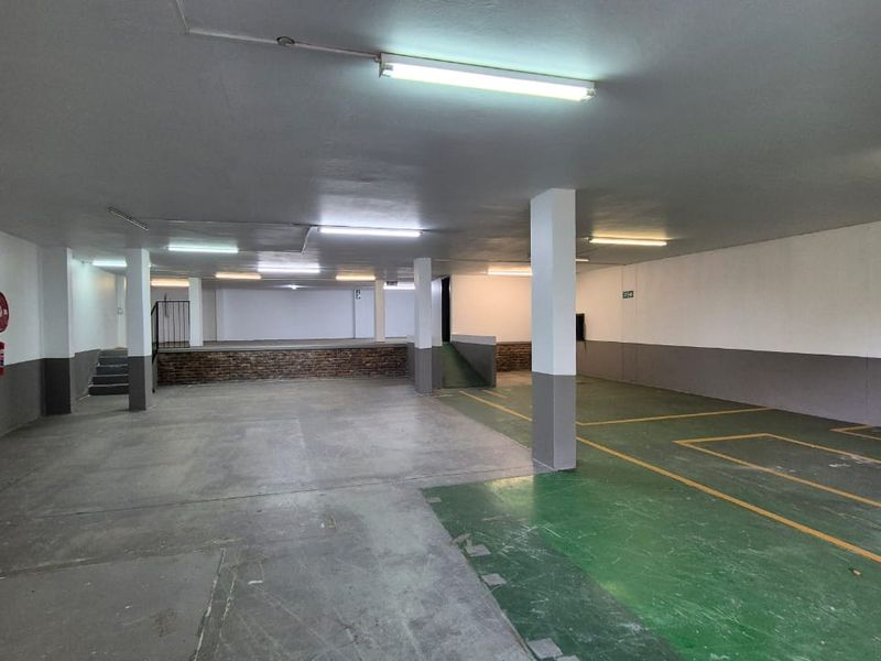 Spacious industrial garage area featuring concrete flooring, structural support columns, and designated parking bays with overhead fluorescent lighting.
