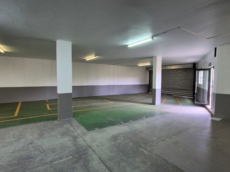 Spacious industrial garage area featuring concrete flooring, structural support columns, fluorescent lighting, and a secure roller shutter door.