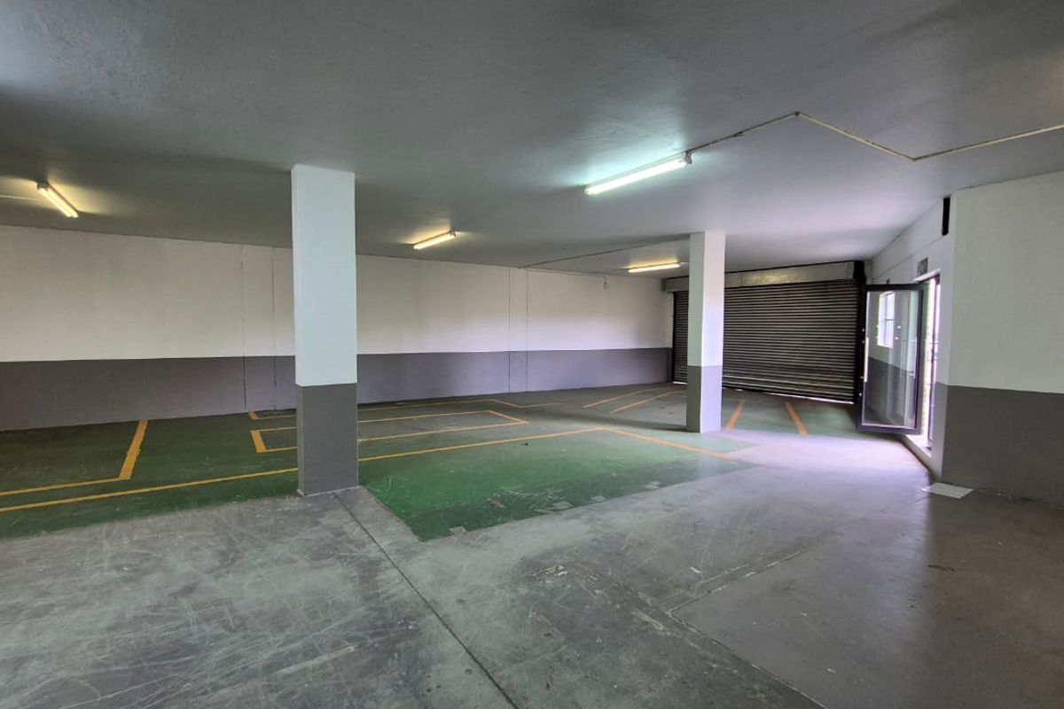 Spacious industrial garage area featuring concrete flooring, structural support columns, fluorescent lighting, and a secure roller shutter door.