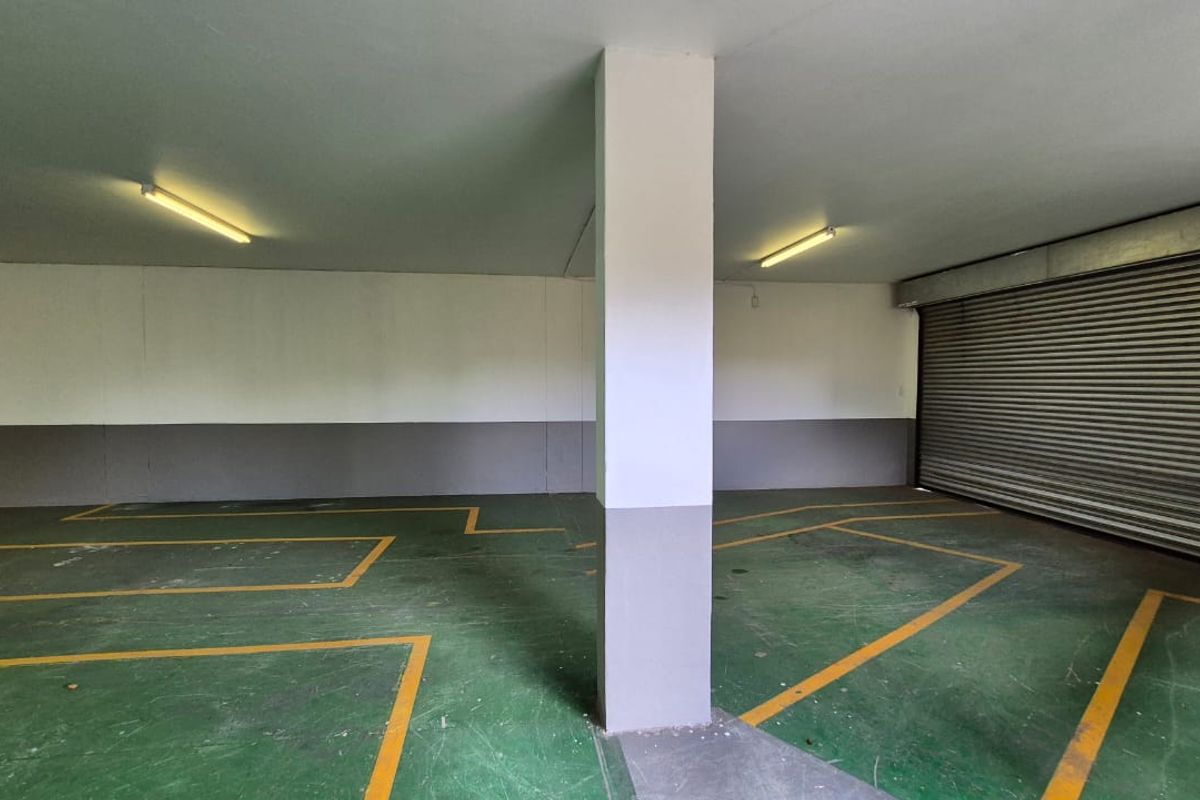 Spacious industrial garage area featuring a roller shutter door, painted concrete flooring with marked parking bays, and overhead fluorescent lighting.