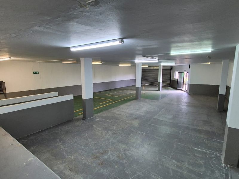 Spacious industrial garage area featuring concrete flooring, support columns, fluorescent lighting, and a roller shutter door, suitable for storage or vehicle parking.