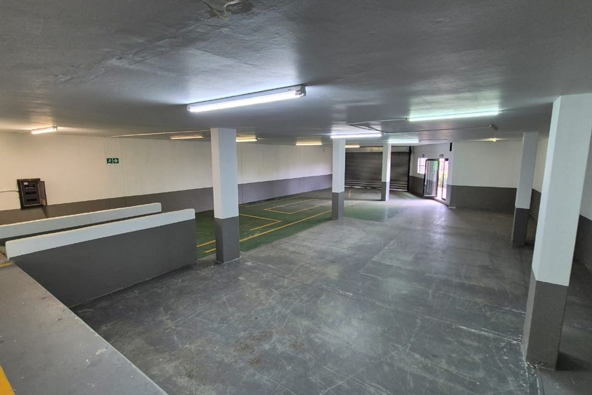 Spacious industrial garage area featuring concrete flooring, support columns, fluorescent lighting, and a roller shutter door, suitable for storage or vehicle parking.