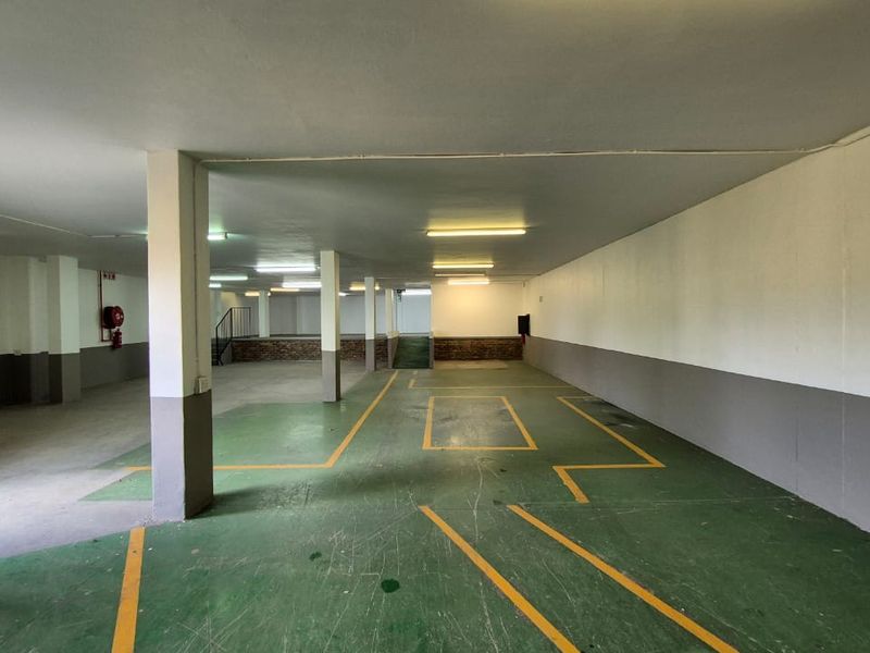 A spacious, open-plan industrial garage area featuring painted concrete flooring with marked bays, structural support columns, and overhead fluorescent lighting.