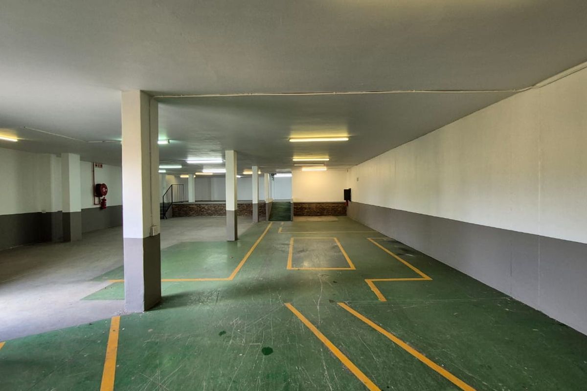 A spacious, open-plan industrial garage area featuring painted concrete flooring with marked bays, structural support columns, and overhead fluorescent lighting.