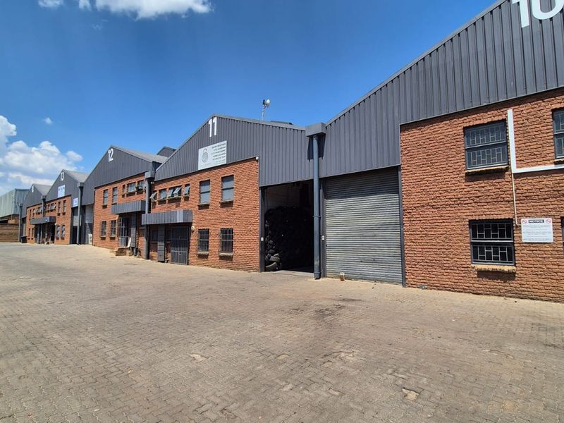 Exterior view of an industrial complex featuring multiple units with brick facades, metal roller shutter doors, and paved driveway access.