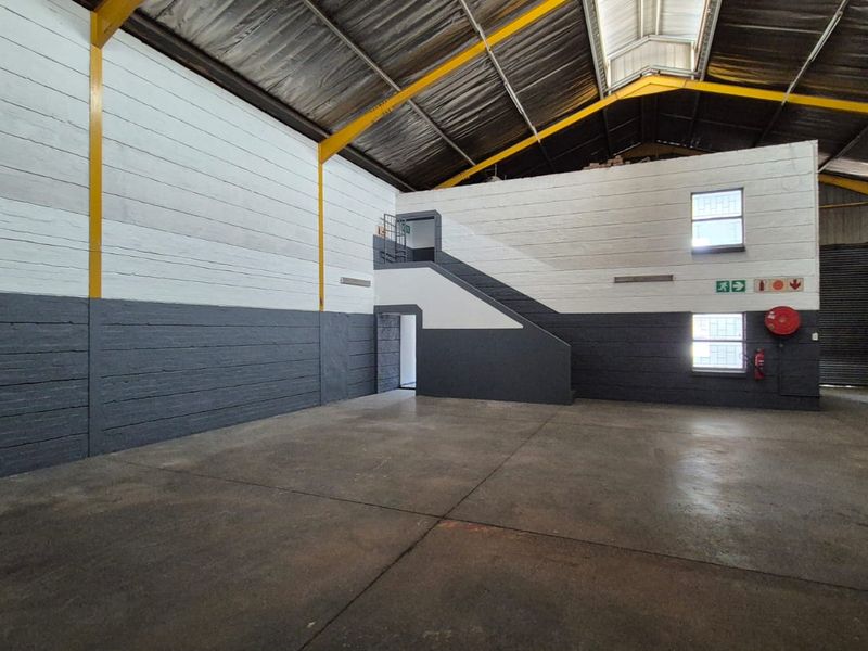 Spacious industrial warehouse unit featuring high ceilings, concrete flooring, a steel portal frame, and an internal staircase leading to an upper level.