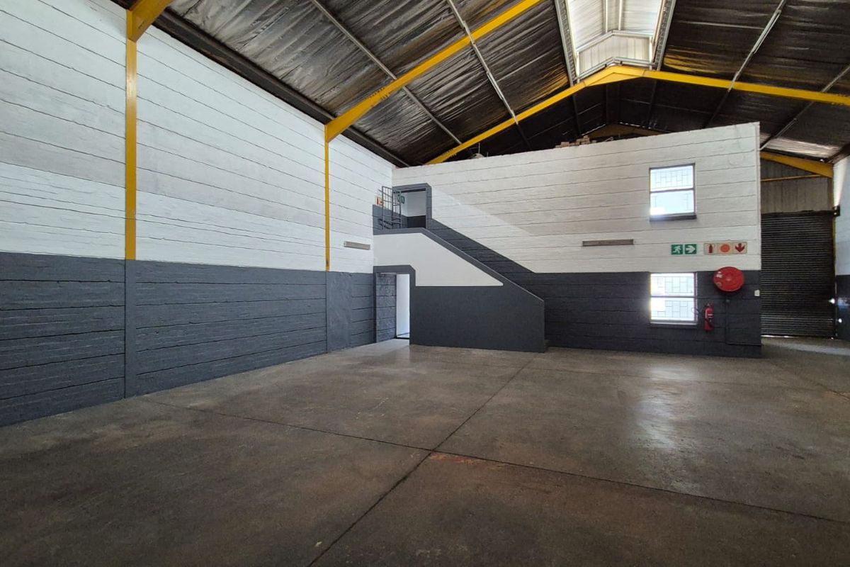 Spacious industrial warehouse unit featuring high ceilings, concrete flooring, a steel portal frame, and an internal staircase leading to an upper level.