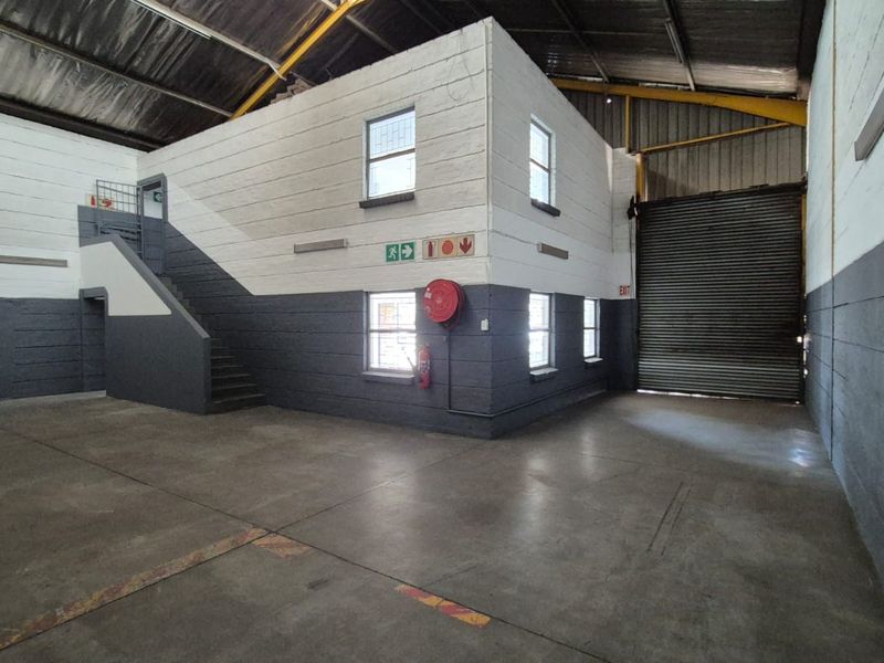 Spacious industrial warehouse unit featuring concrete flooring, high ceilings with exposed steel trusses, a roller shutter door, and an internal office or storage structure.