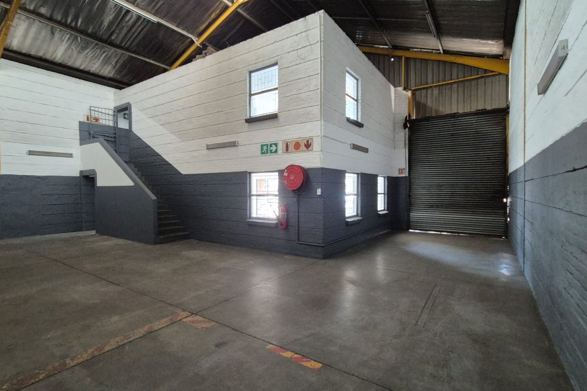 Spacious industrial warehouse unit featuring concrete flooring, high ceilings with exposed steel trusses, a roller shutter door, and an internal office or storage structure.