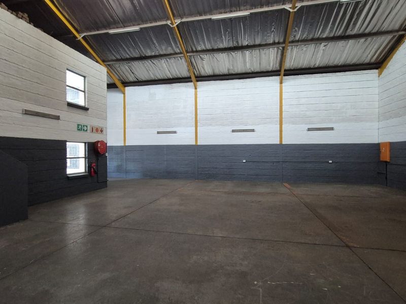 Spacious industrial utility area featuring high ceilings with exposed steel trusses, durable concrete flooring, and painted masonry walls.