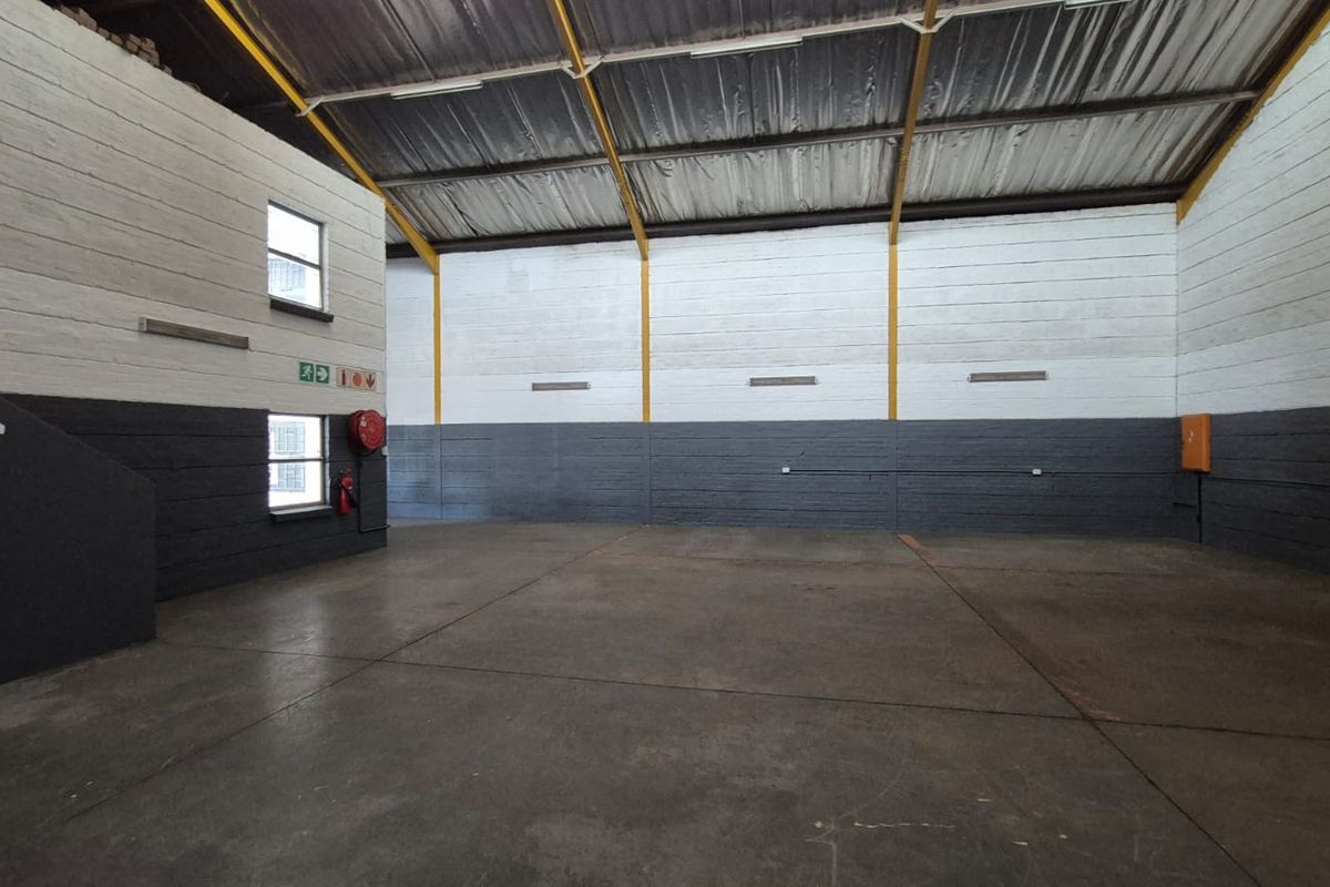 Spacious industrial utility area featuring high ceilings with exposed steel trusses, durable concrete flooring, and painted masonry walls.