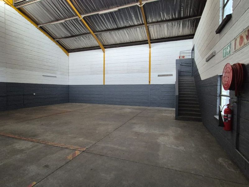 Spacious industrial warehouse unit featuring high ceilings with exposed steel trusses, concrete flooring, and integrated fire safety equipment.