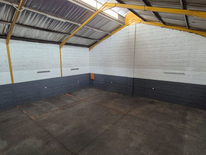 Spacious industrial garage or workshop area featuring exposed steel roof trusses, painted brick walls, and durable concrete flooring.