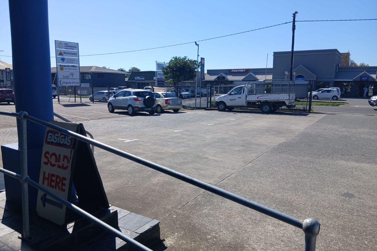 A commercial exterior view showing a paved parking area, security fencing, and various business signage for the office park.
