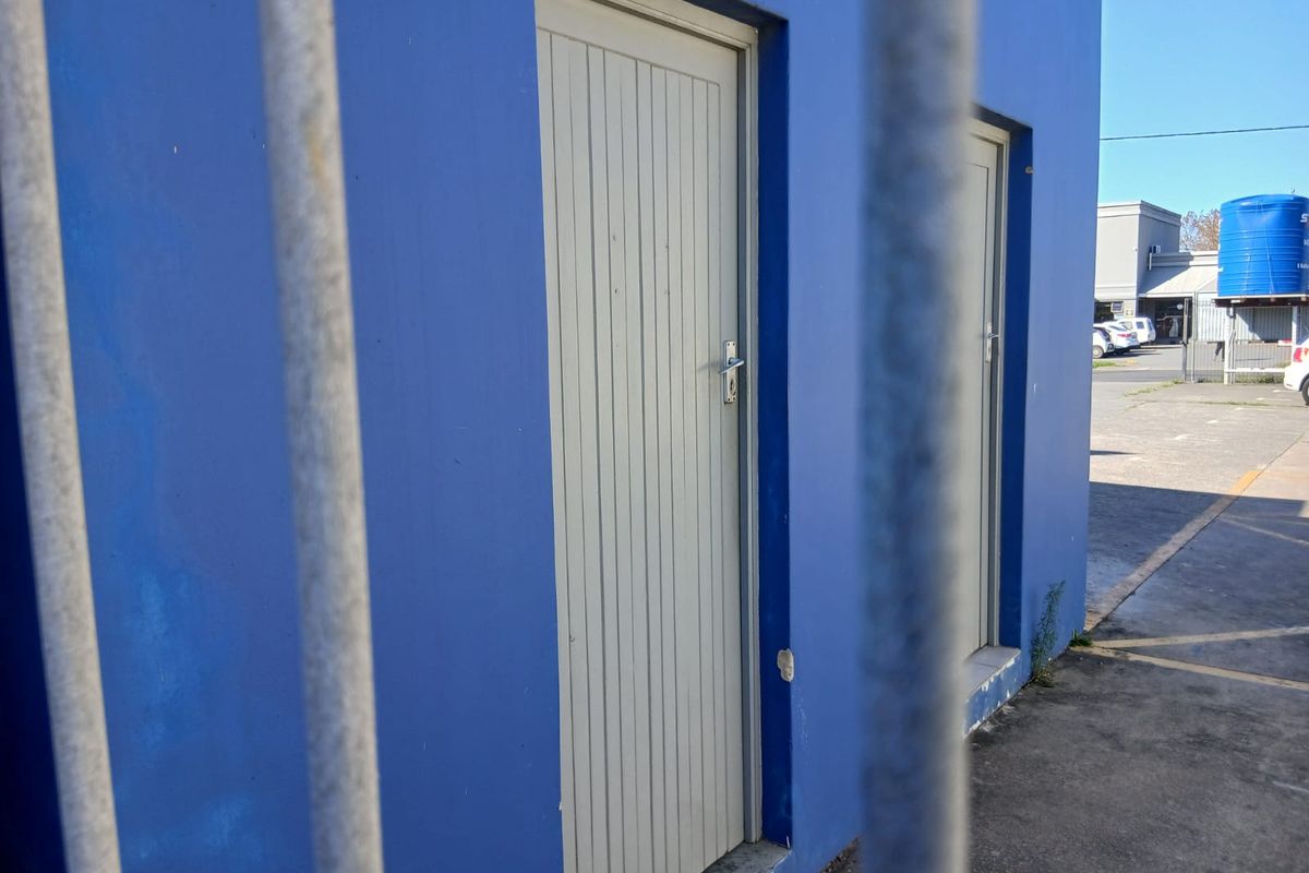 Exterior view of a commercial building featuring blue painted walls and two vertical panel doors, viewed through metal security bars.