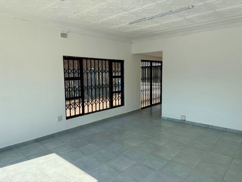 A vacant commercial office space featuring tiled flooring, decorative ceiling tiles, and secure window and door access with fitted security gates.