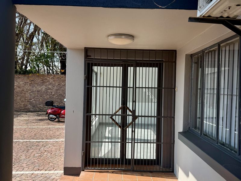 Commercial building entrance featuring a secure metal gate, tiled step, and exterior air conditioning unit, situated adjacent to a paved parking area.