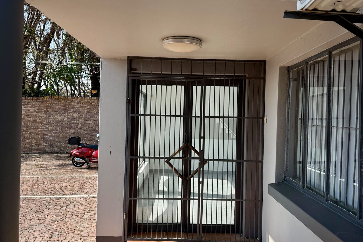 Commercial building entrance featuring a secure metal gate, tiled step, and exterior air conditioning unit, situated adjacent to a paved parking area.
