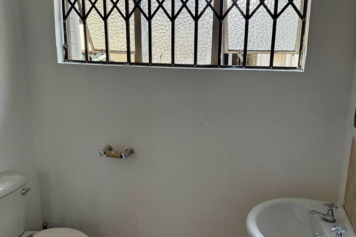 A functional bathroom featuring a pedestal basin, toilet, and a window fitted with a security gate.