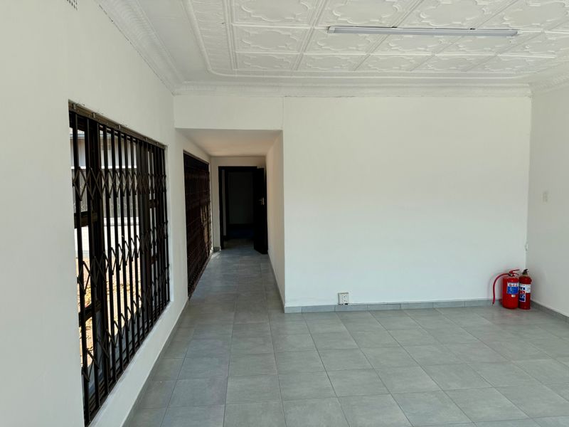 An empty, well-maintained commercial space featuring tiled flooring, decorative ceiling tiles, and secure window gates, suitable for office or retail use.