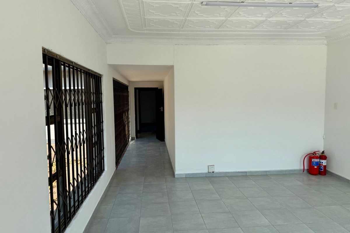 An empty, well-maintained commercial space featuring tiled flooring, decorative ceiling tiles, and secure window gates, suitable for office or retail use.