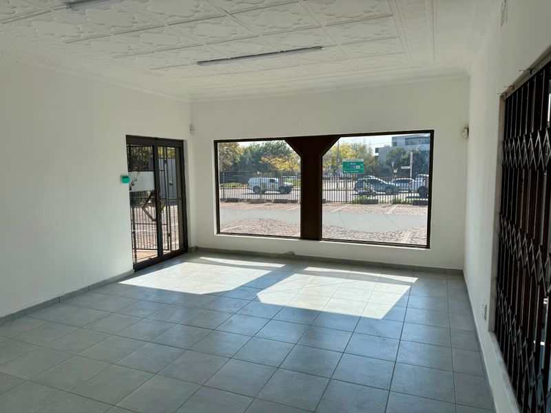 A vacant commercial office space featuring tiled flooring, decorative ceiling tiles, and a large street-facing display window with security gates.