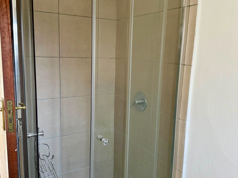 A functional bathroom shower enclosure featuring tiled walls and a mosaic-style tiled floor, presenting a standard, dated aesthetic.