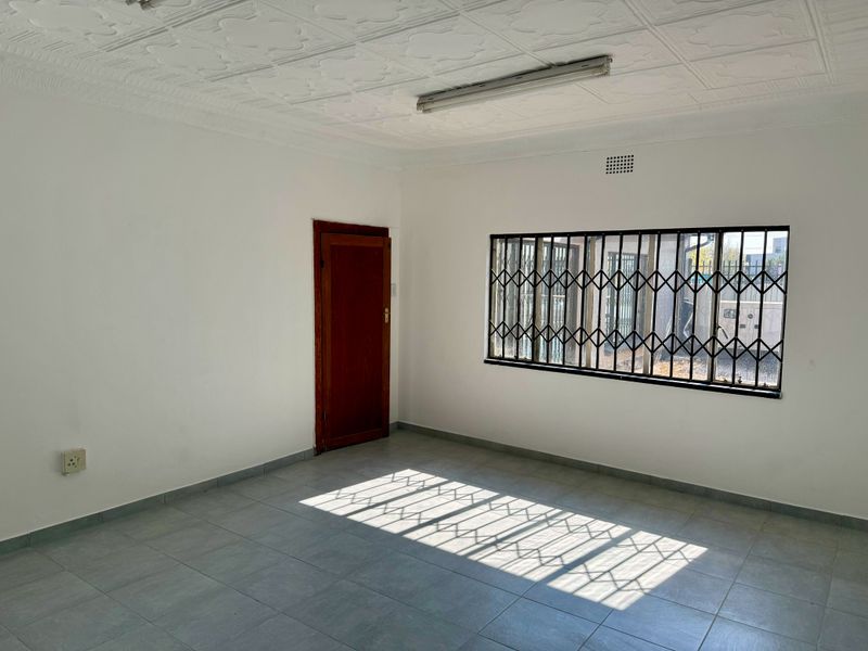 A vacant, well-lit office space featuring tiled flooring, decorative ceiling tiles, and a window fitted with a security gate.