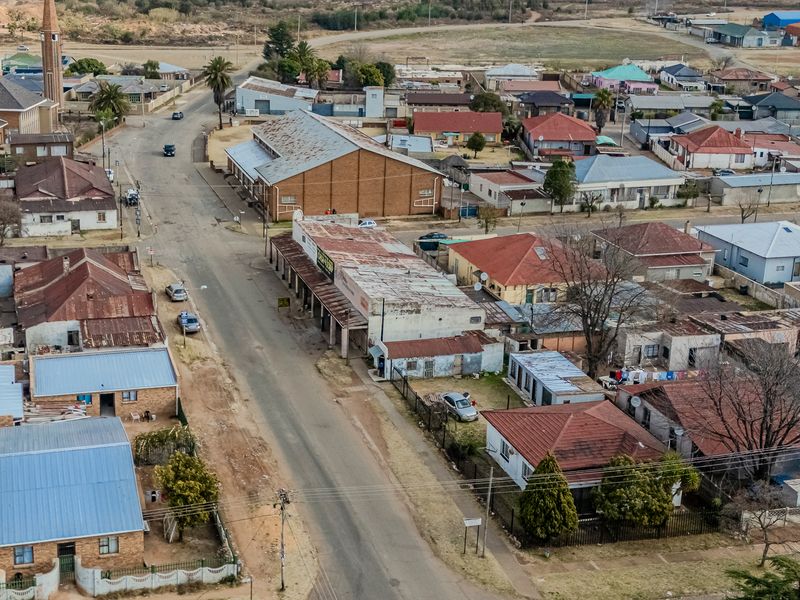 Aerial view of a commercial and residential street block featuring various building structures with metal and tiled roofing in a suburban setting.