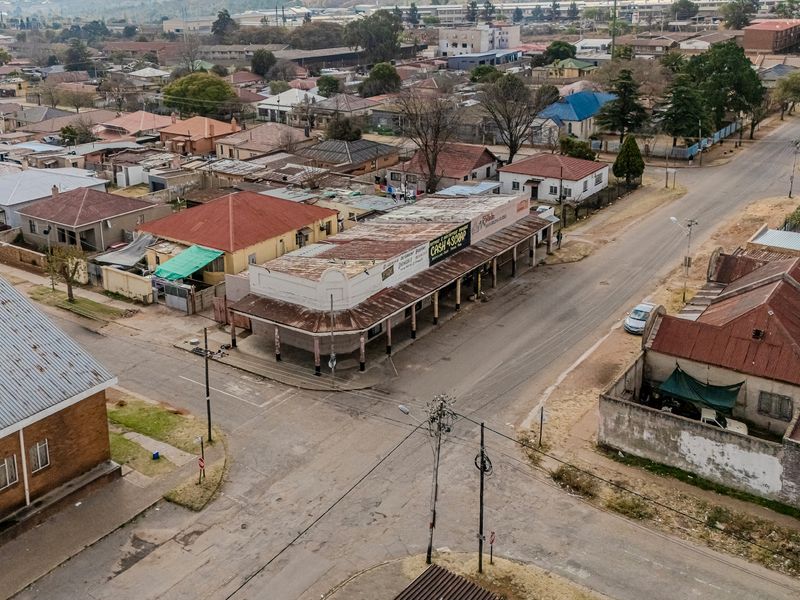 Aerial view of a corner commercial office building featuring a covered sidewalk and a weathered corrugated metal roof in a suburban setting.