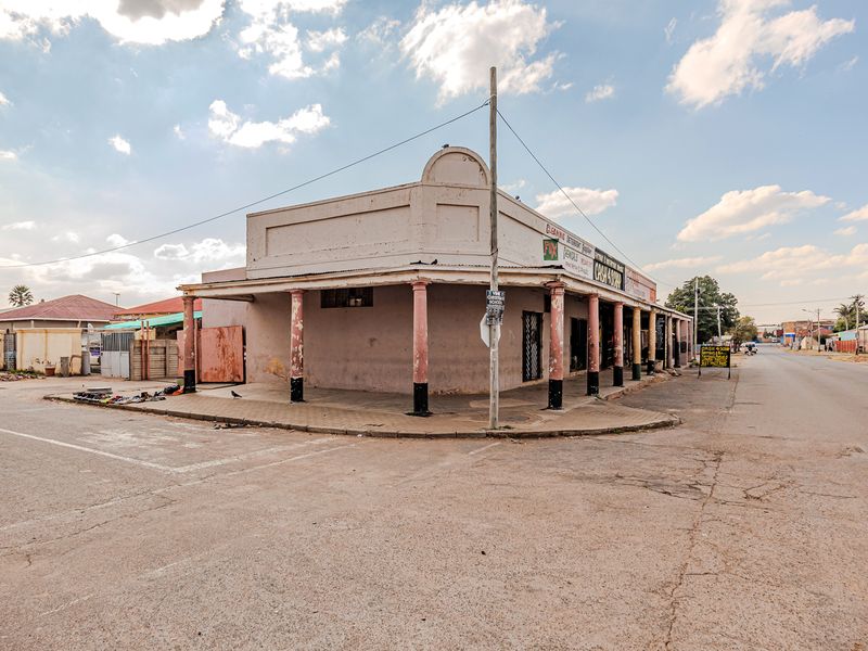 Corner commercial office building featuring a covered veranda with structural columns, located on a street corner with visible exterior wear.