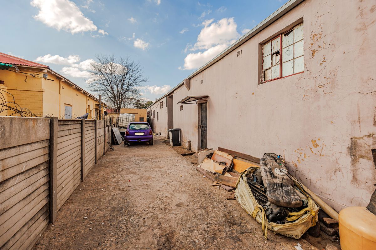 Rear exterior view of the office property showing a concrete driveway, boundary wall, and building facade with visible wear and maintenance requirements.