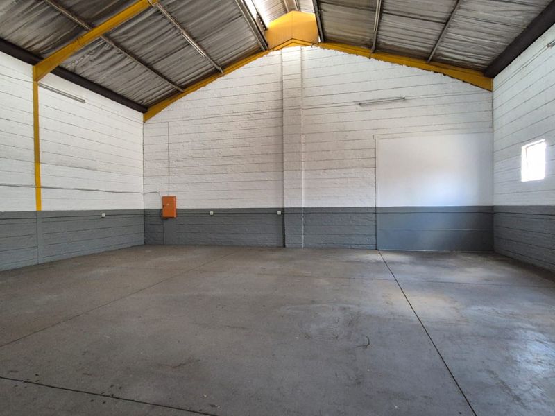 Spacious industrial utility area featuring high ceilings with exposed steel trusses, durable concrete flooring, and painted masonry walls, suitable for storage or workshop use.