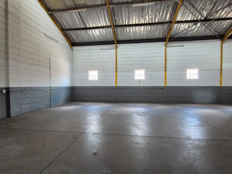 Spacious industrial warehouse unit featuring high ceilings with exposed steel trusses, durable concrete flooring, and painted brick walls.