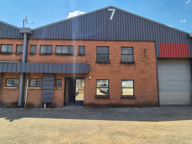 Front elevation of an industrial unit featuring a brick facade, metal roller shutter door, and paved driveway access.