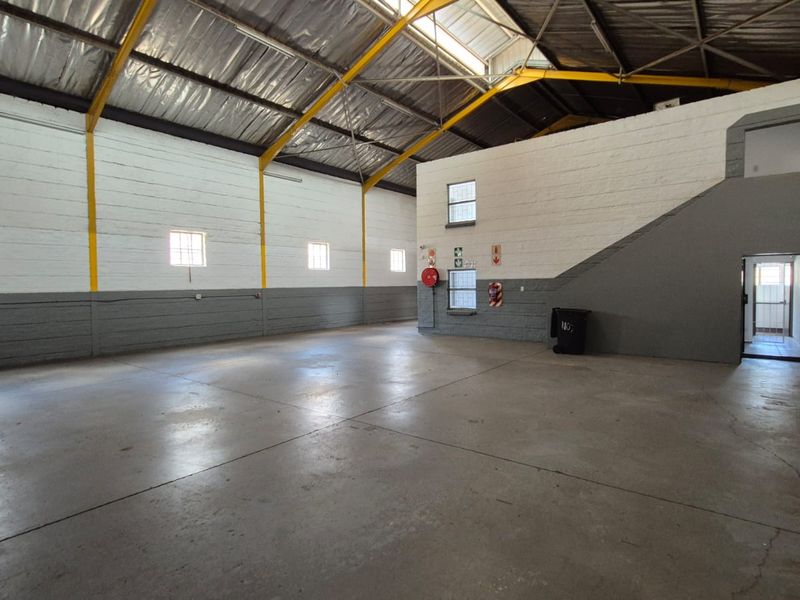 Spacious industrial utility area featuring high ceilings with exposed steel trusses, concrete flooring, and painted brick walls, suitable for warehouse or workshop use.