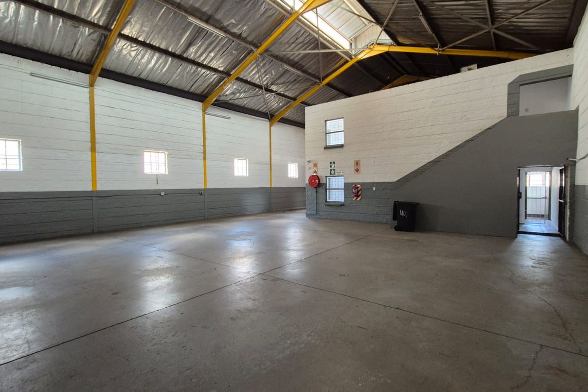 Spacious industrial utility area featuring high ceilings with exposed steel trusses, concrete flooring, and painted brick walls, suitable for warehouse or workshop use.