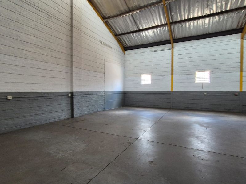 A spacious, empty industrial utility area featuring painted brick walls, durable concrete flooring, and high-clearance exposed steel roof trusses.