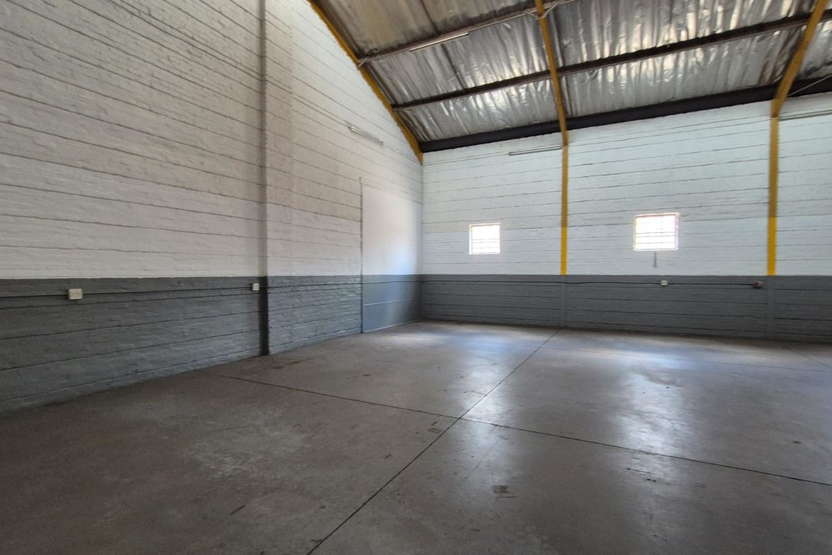 A spacious, empty industrial utility area featuring painted brick walls, durable concrete flooring, and high-clearance exposed steel roof trusses.