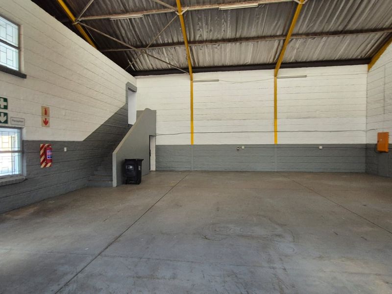 Spacious industrial warehouse unit featuring high ceilings with exposed steel trusses, concrete flooring, and integrated fire safety equipment.