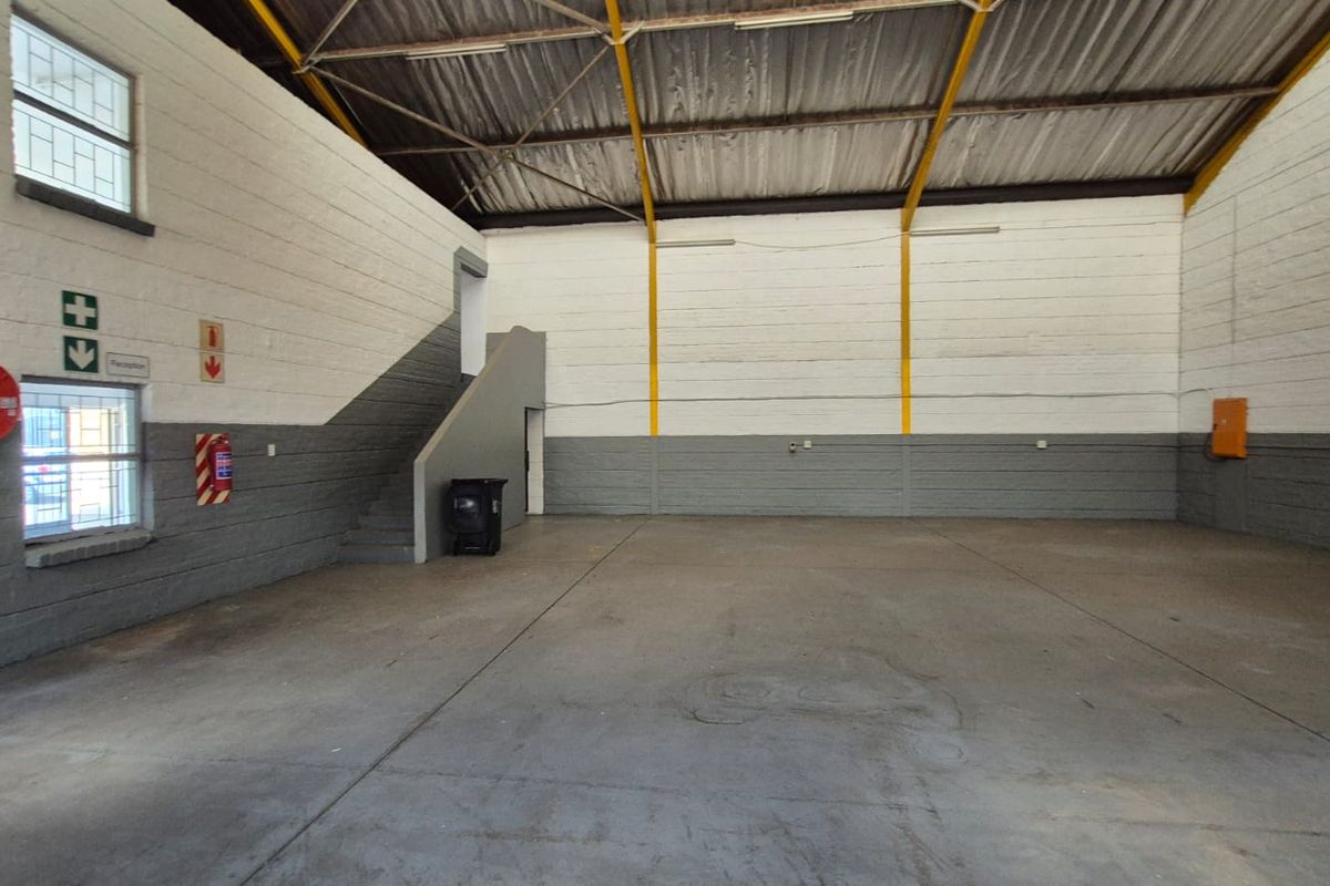Spacious industrial warehouse unit featuring high ceilings with exposed steel trusses, concrete flooring, and integrated fire safety equipment.