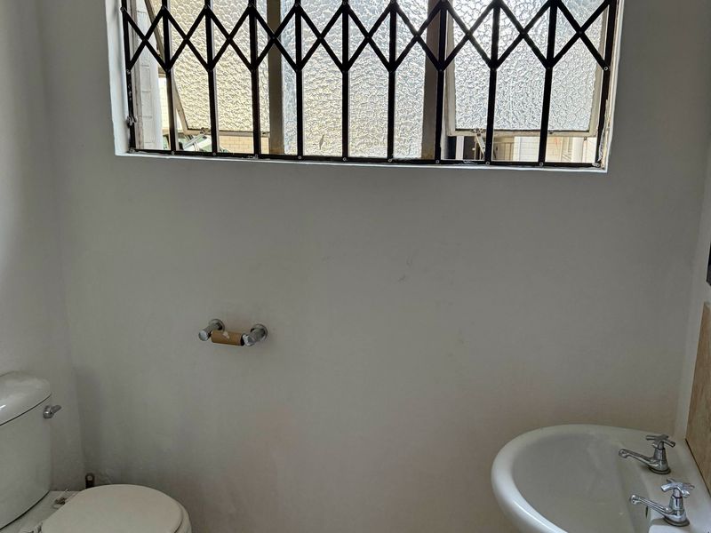 A functional bathroom featuring a pedestal basin, toilet, and a window fitted with a security gate.