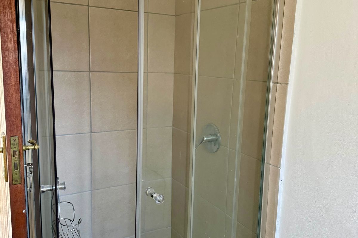 A functional bathroom shower enclosure featuring tiled walls and a mosaic-style tiled floor, presenting a standard, dated aesthetic.