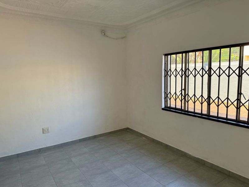 A clean, empty bedroom featuring neutral tiled flooring, a security gate on the window, and decorative ceiling cornicing.