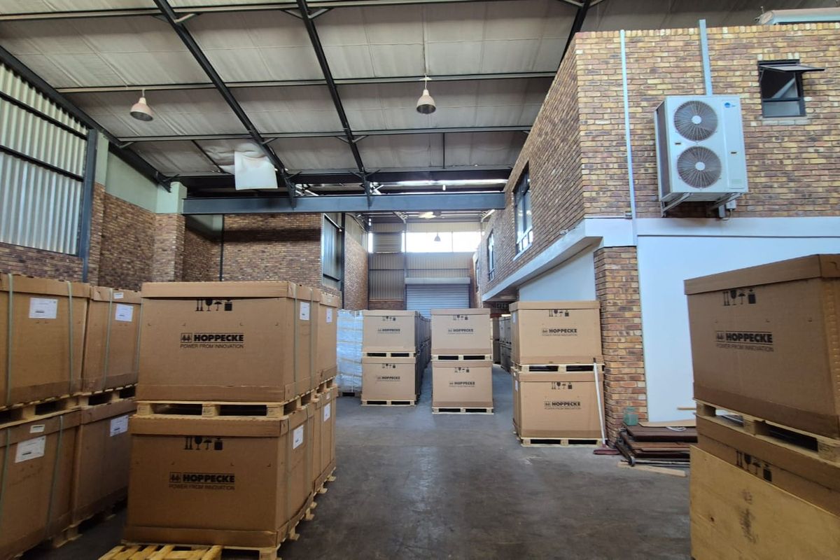 Spacious industrial warehouse featuring high ceilings with exposed steel trusses, face brick walls, concrete flooring, and a roller shutter door.